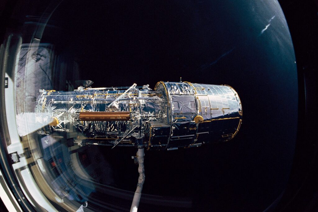 El telescopio espacial Hubble en órbita terrestre, con sus paneles solares desplegados sobre el fondo negro
