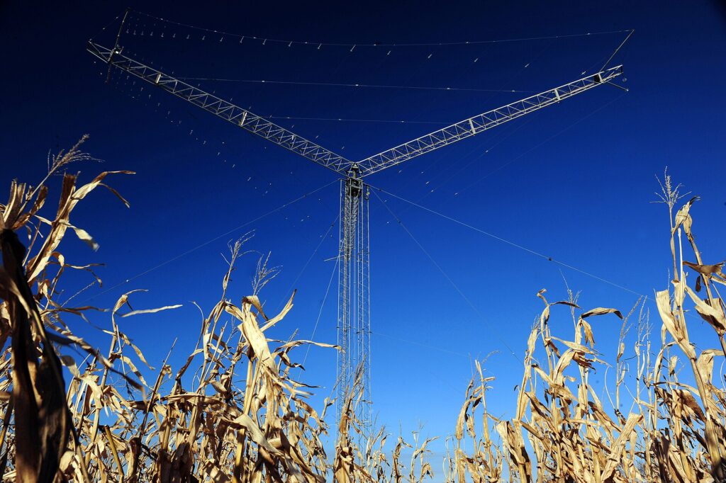Antena metálica de brazos cruzados clavada en suelo rojo bajo un cielo sin nubes