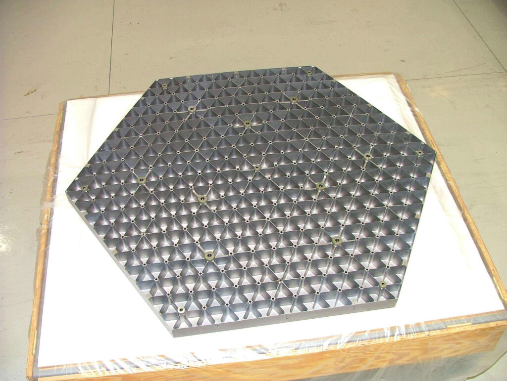Segmento hexagonal de espejo pulido reflejando el entorno del taller donde se fabrica