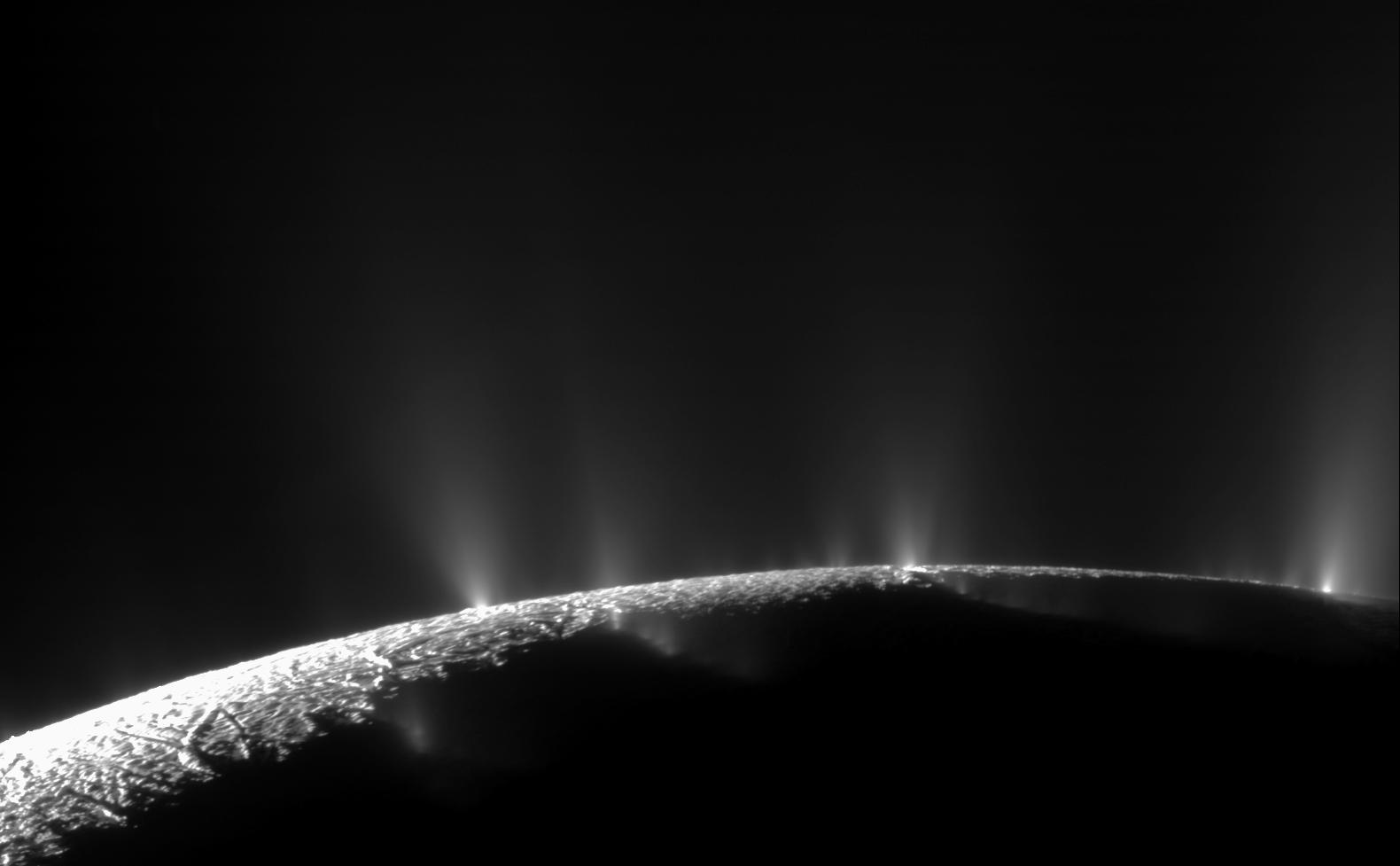 Columnas de hielo brotando del polo sur de Encélado iluminadas a contraluz sobre el fondo oscuro