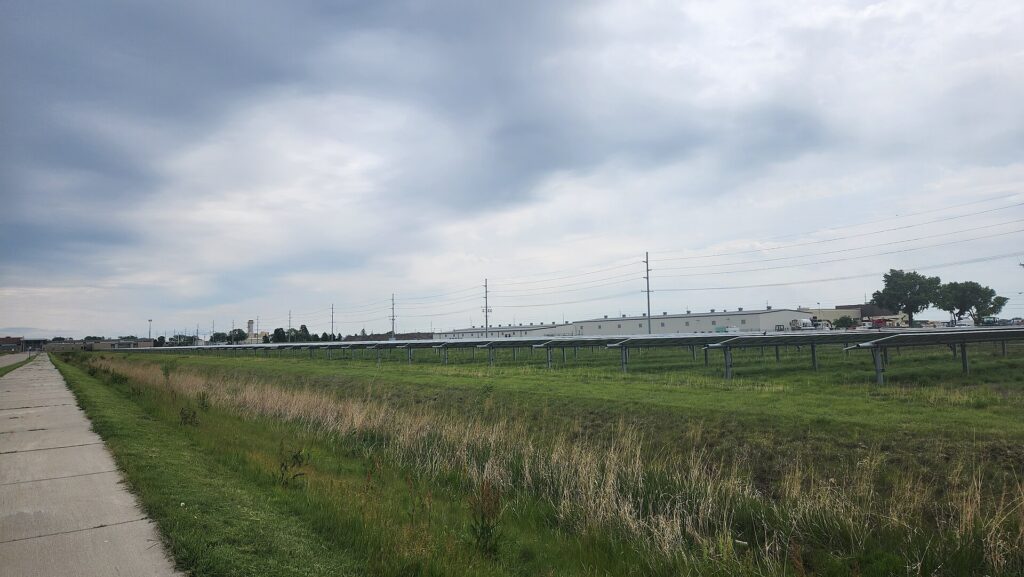 Hileras de paneles fotovoltaicos sobre terreno llano con torres de transporte eléctrico al fondo