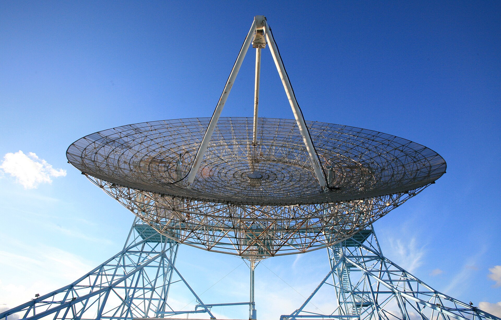 Gran antena parabólica de un radiotelescopio orientada hacia el cielo sobre un terreno despejado