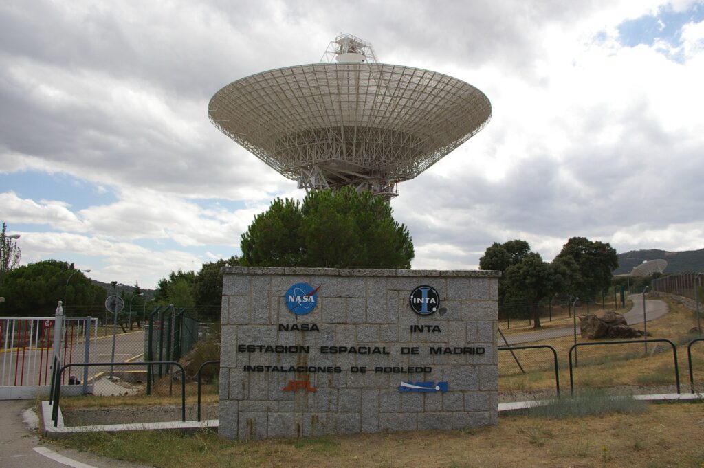 Gran antena parabólica de seguimiento apuntando al cielo desde una explanada rodeada de colinas