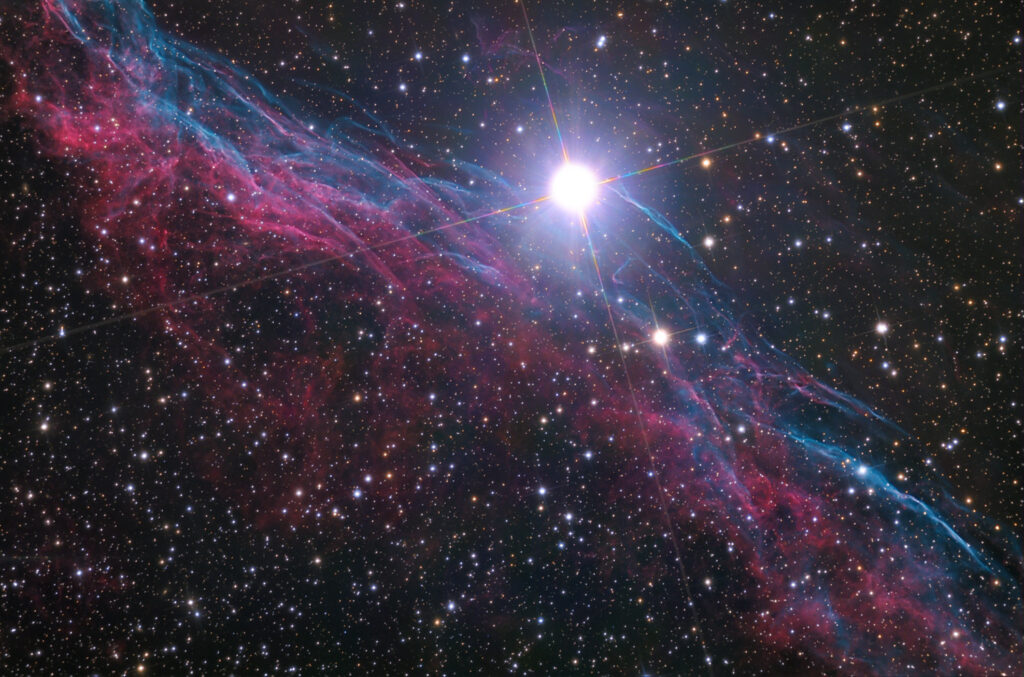 Resto de supernova con filamentos delgados y coloreados expandiéndose sobre un campo de estrellas