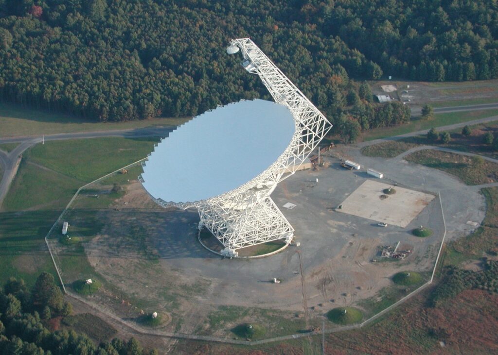 Radiotelescopio de gran tamaño con su montura móvil rodeado de bosque y colinas boscosas