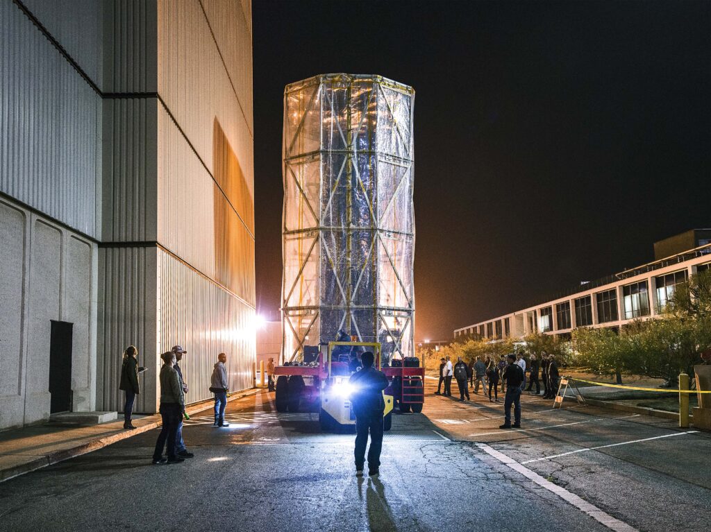 Sonda espacial en sala limpia rodeada de técnicos con trajes blancos y equipos de montaje