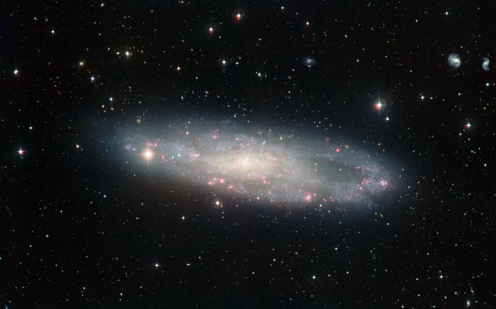 Galaxia espiral con brazos salpicados de regiones brillantes de formación estelar y un bulbo central amarillento