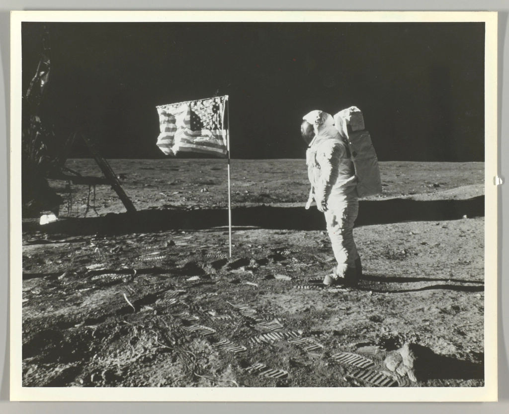 Astronauta junto a una bandera clavada sobre el suelo lunar polvoriento con la Tierra al fondo