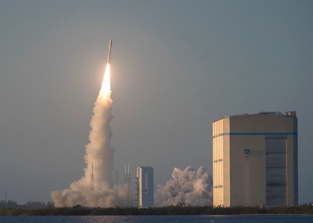 Despegue nocturno de un cohete Atlas V con la columna de llama iluminando la torre de lanzamiento